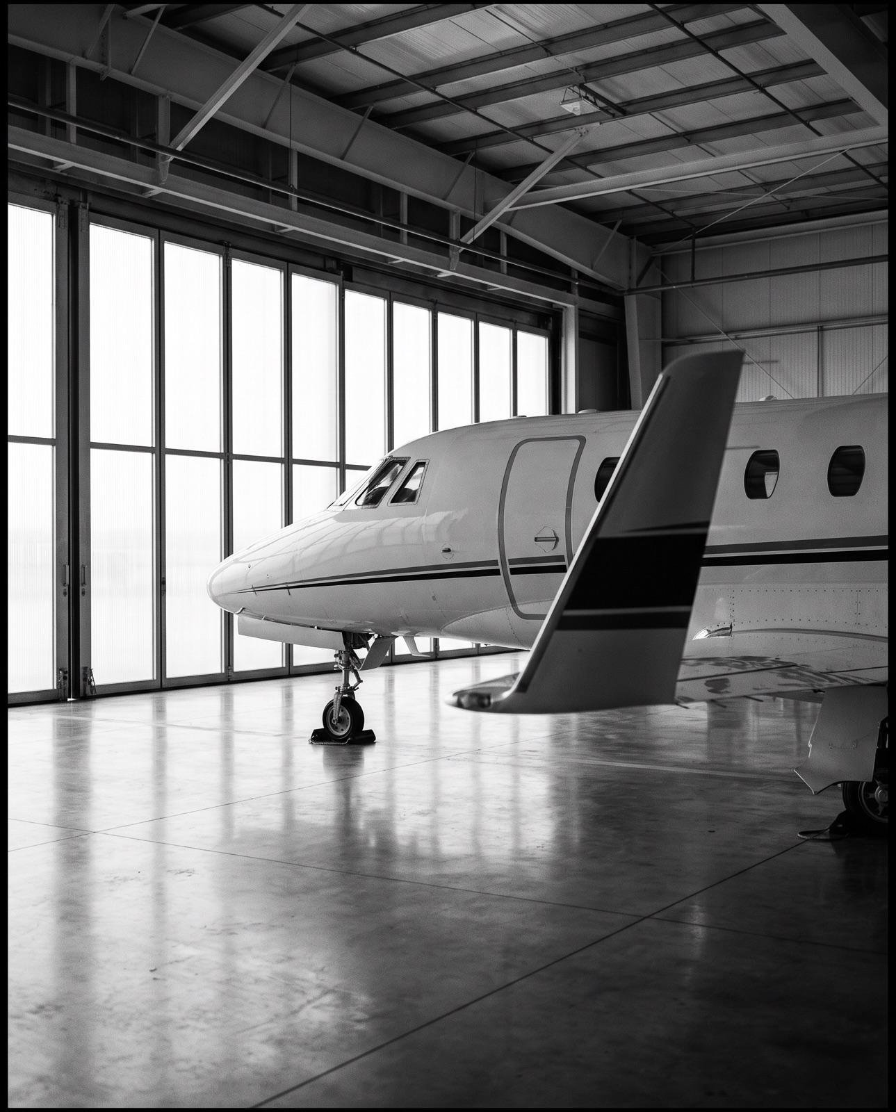 Nose and wing of a business jet inside a hangar, in black and white